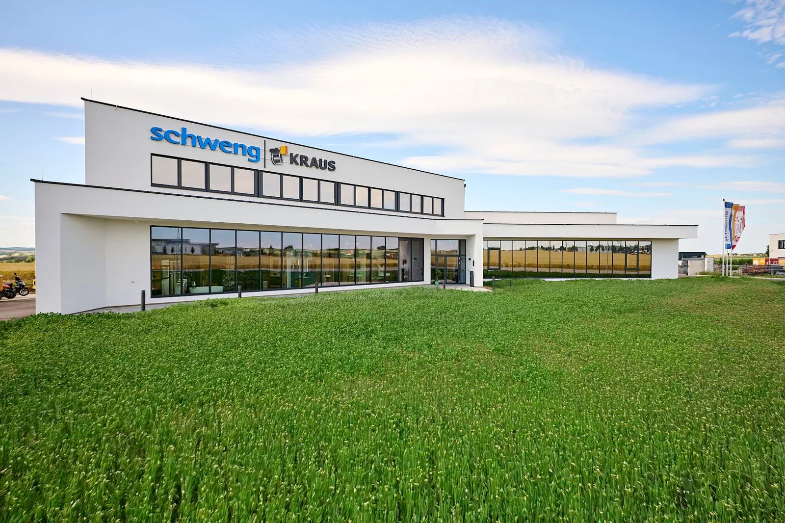 Firmengebäude von der Wiese aus, Glasfront im Erdgeschoss und Schriftzug schweng und KRAUS