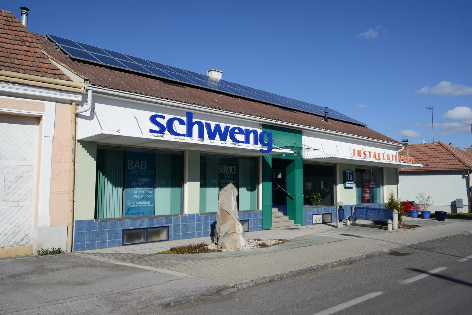 Geschäft mit großem blauem Schriftzug schweng, Schaufenstern und Photovoltaik auf dem Dach
