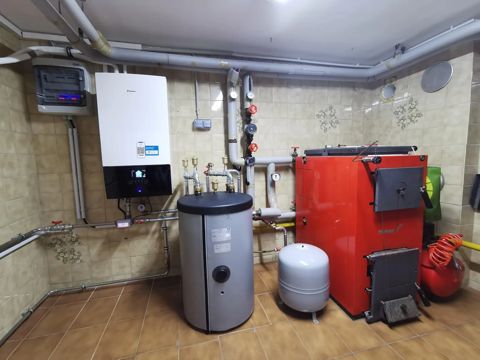 Heizraum mit neuem Wärmepumpen-Innengerät an der Wand, Speicher, Ausdehnungsgefäß und rotem Holzkessel