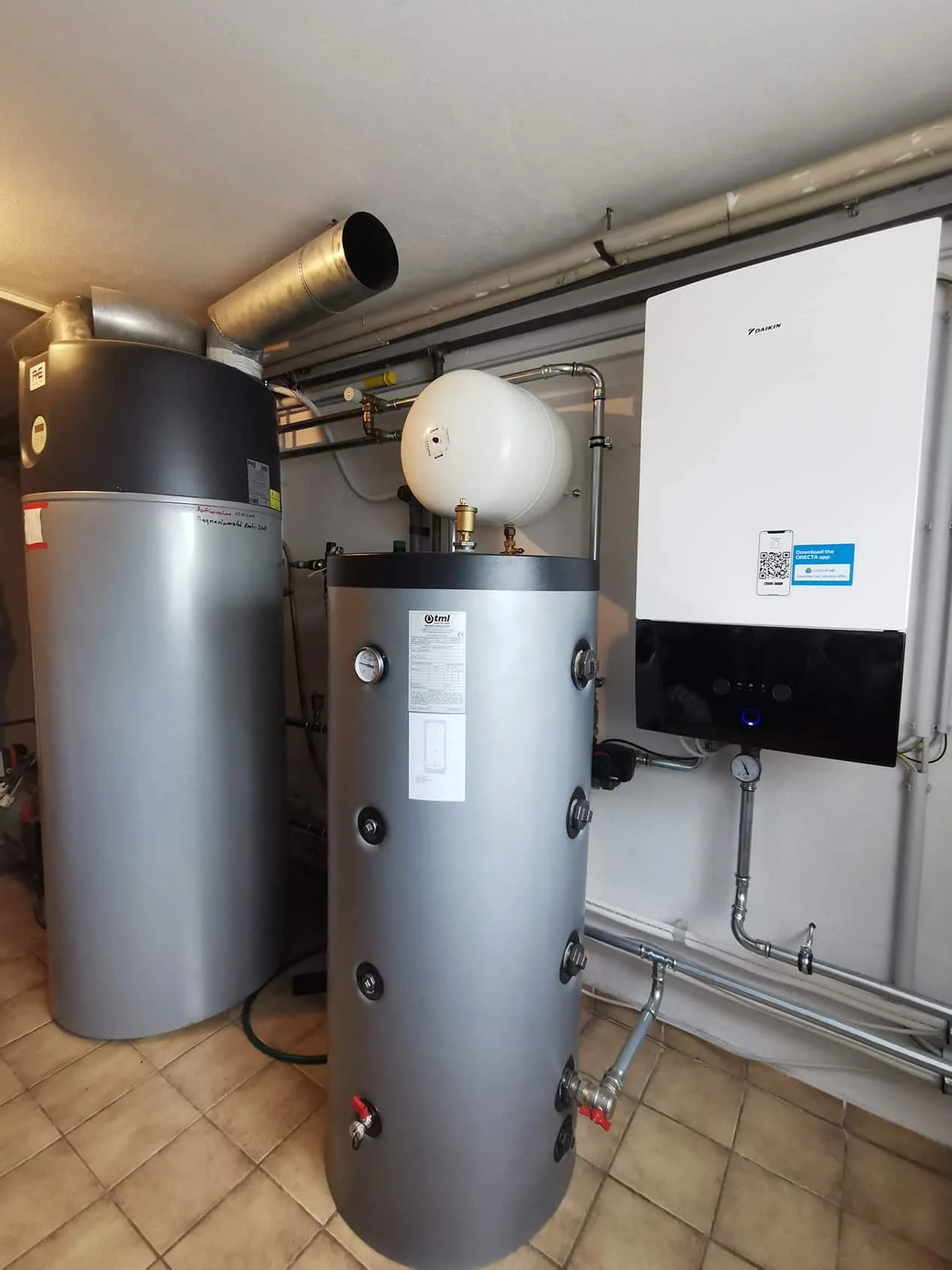 Warmwasserboiler, Pufferspeicher und weißes Innengerät an der Wand in einem gefliesten Keller