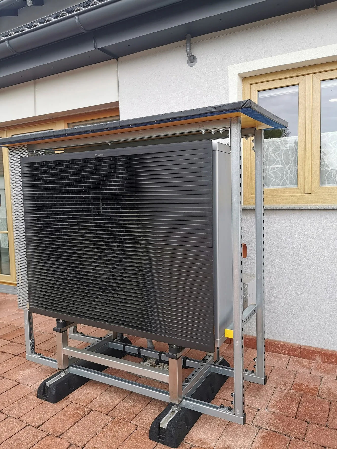 Außengerät einer Luftwärmepumpe auf einem Metallgestell vor einem Haus