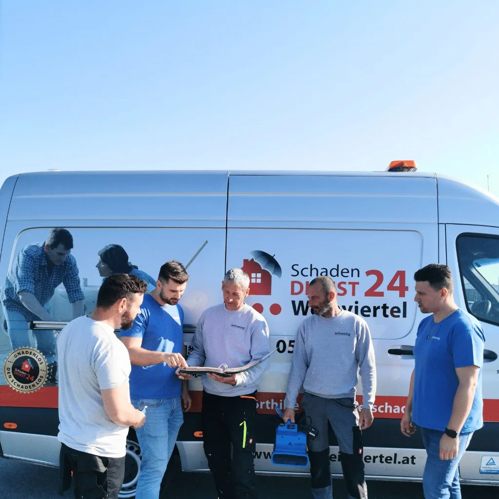 Fünf Männer vom Schadendienst-Team besprechen sich vor dem beschrifteten Einsatzwagen Schaden Dienst 24 Weinviertel