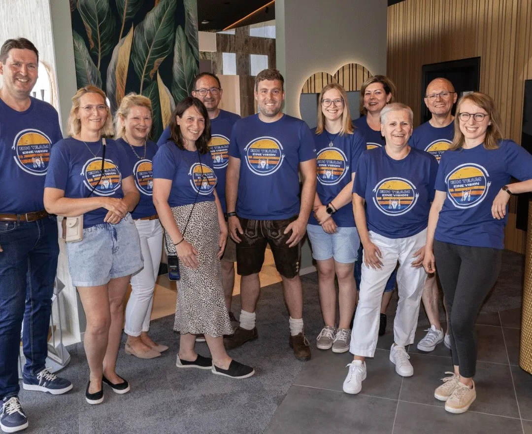 Elf Mitarbeiterinnen und Mitarbeiter in blauen Team-Shirts mit dem Aufdruck Ein Team eine Vision im Schauraum